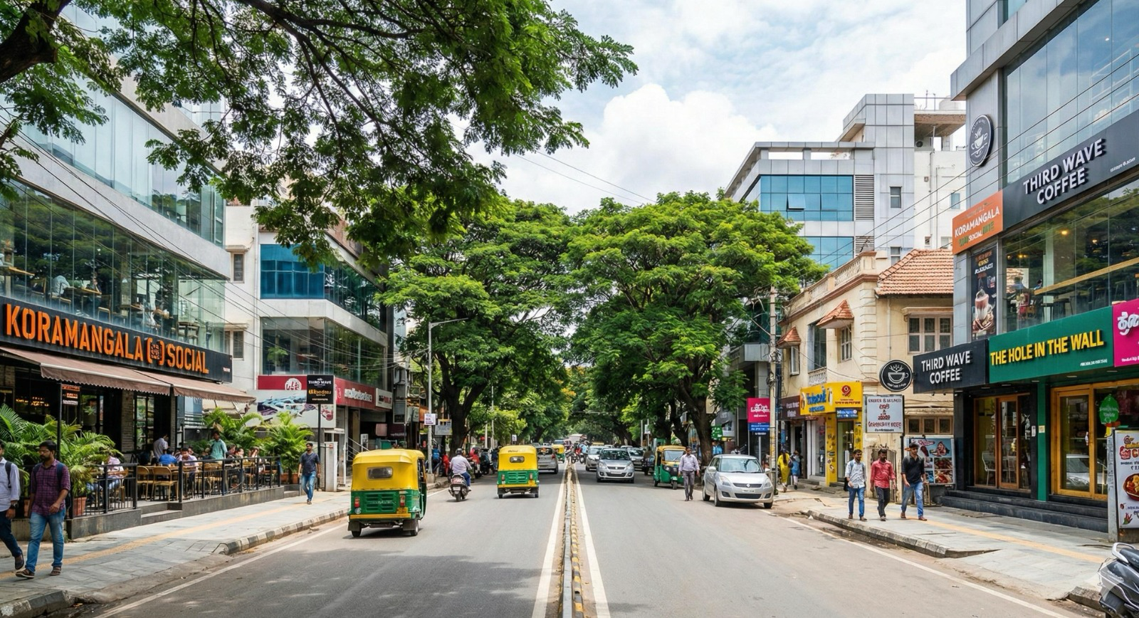 Tree-lined street in Koramangala, Bengaluru lined with cafes, shops and auto-rickshaws